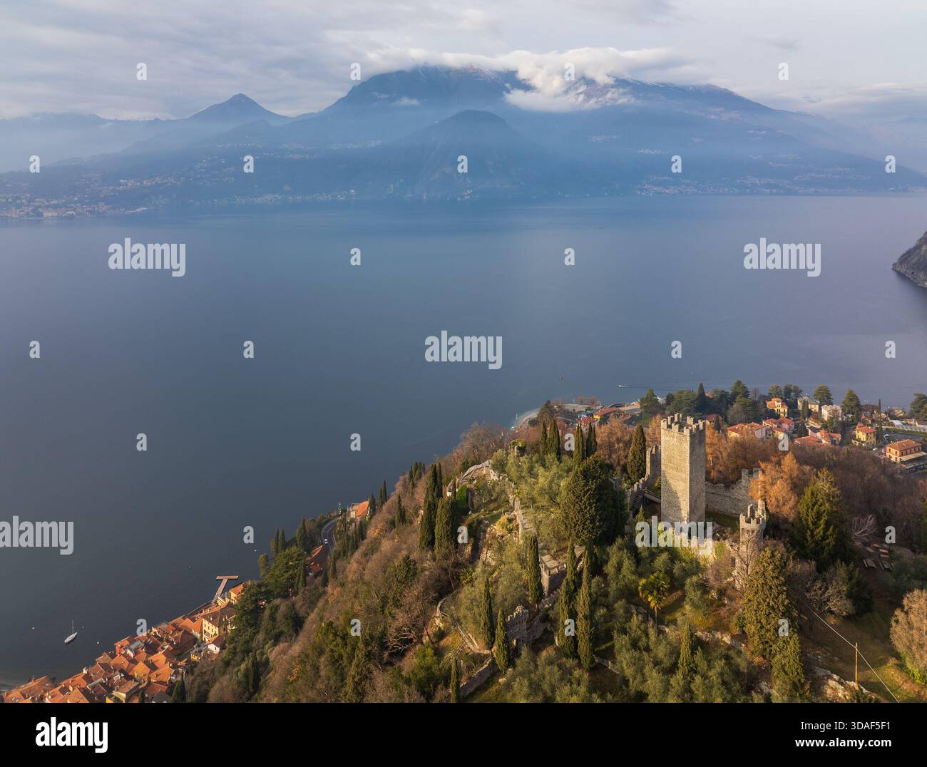 Veduta aerea del Castello di Vezio in piedi a guardia delle tranquille acque, una fortezza contro i secoli, con montagne ricoperte di nebbia, Varenna, Lombar Foto Stock