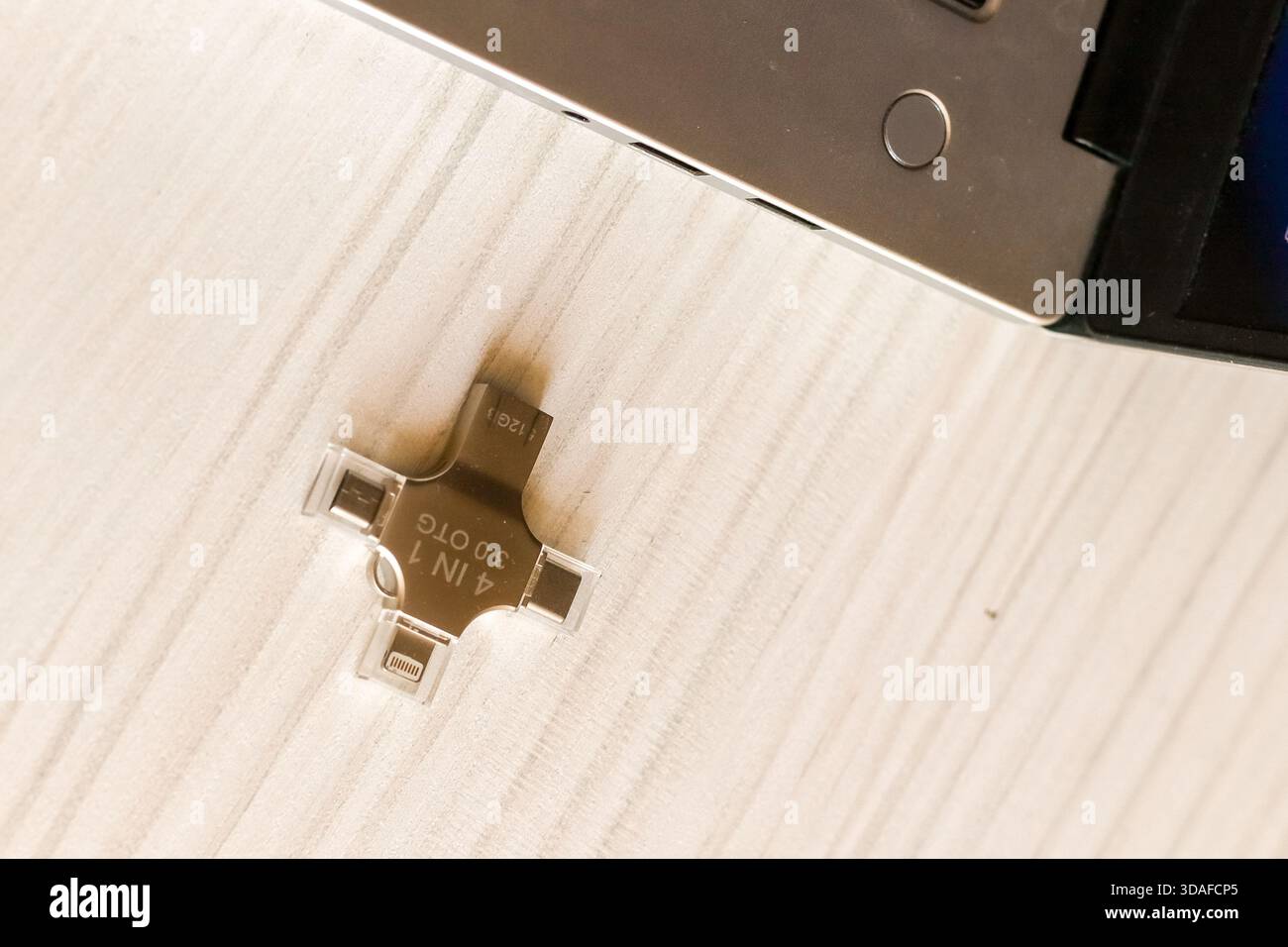 Unità USB multifunzione posizionata accanto a un computer portatile color argento con schermo aperto su un tavolo in legno chiaro, pronta per l'uso e il collegamento dati immediati. Foto Stock