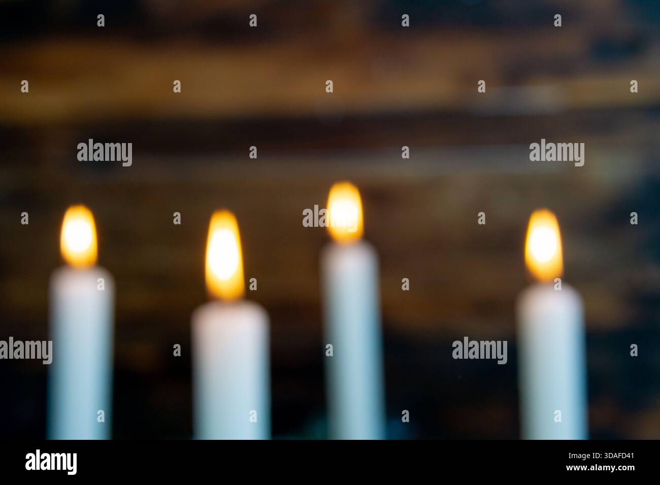 Quattro fiamme calde appaiono leggermente sfocate su uno sfondo rustico in legno, creando un'atmosfera da sogno e suggestiva dell'avvento. Foto Stock