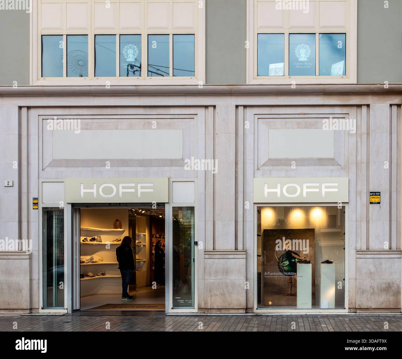 Negozio di scarpe HOFF esterno con grandi finestre, Malaga, Spagna. Espositore di scarpe e accessori, singolo cliente all'interno. Facciata in pietra di stile moderno. Foto Stock