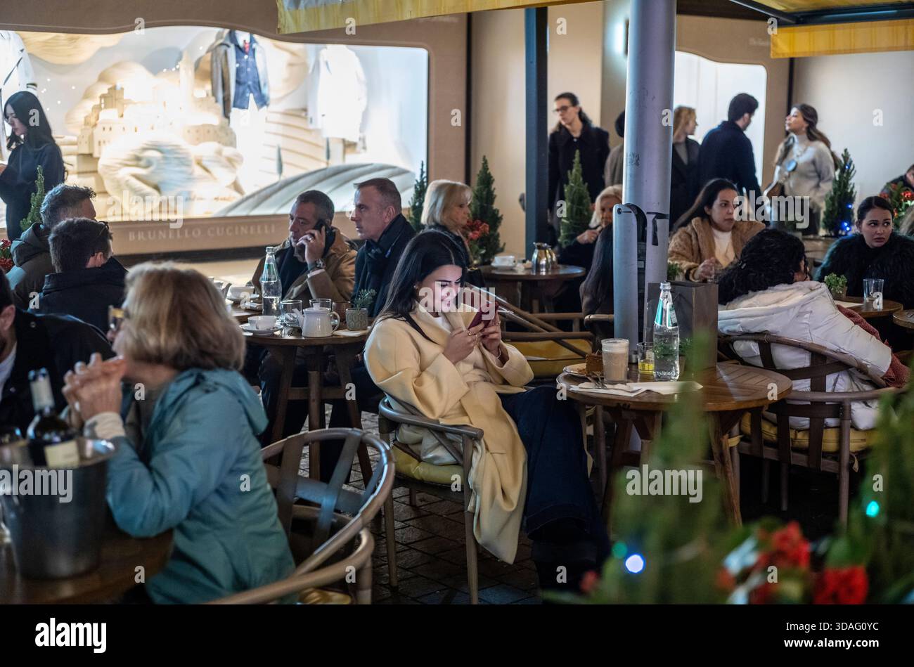 Una donna attraente che usa il suo smartphone mentre si siede al tavolo di un ristorante esterno fuori dai grandi magazzini Harrods di lusso, Knightsbridge, Londra, Regno Unito Foto Stock