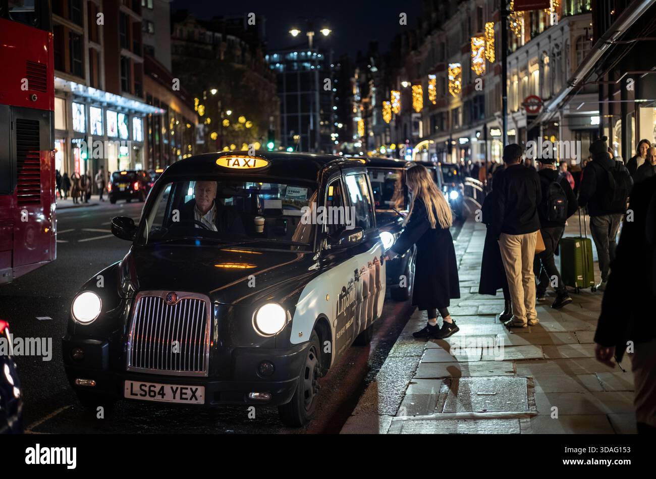 I turisti apprezzano le luci natalizie fuori Harrods su Brompton Road, nella ricca zona di Knightsbridge nel centro di Londra, Inghilterra, Regno Unito Foto Stock