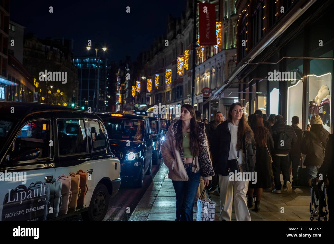 I turisti apprezzano le luci natalizie fuori Harrods su Brompton Road, nella ricca zona di Knightsbridge nel centro di Londra, Inghilterra, Regno Unito Foto Stock