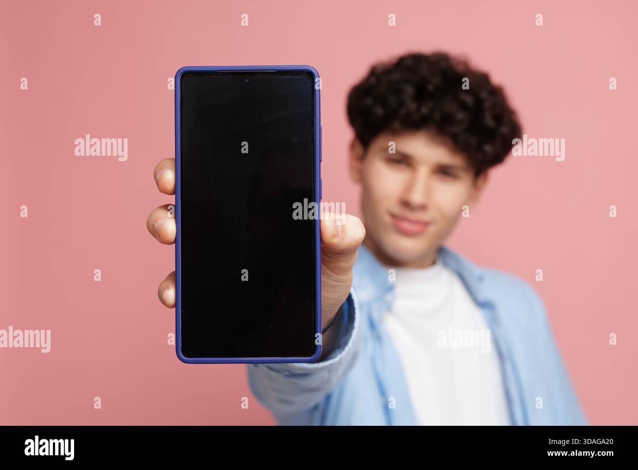 Ritratto di un giovane che mostra uno smartphone moderno con schermo nero vuoto su sfondo rosa ideale per il mockup di servizi online di social media di app mobili Foto Stock