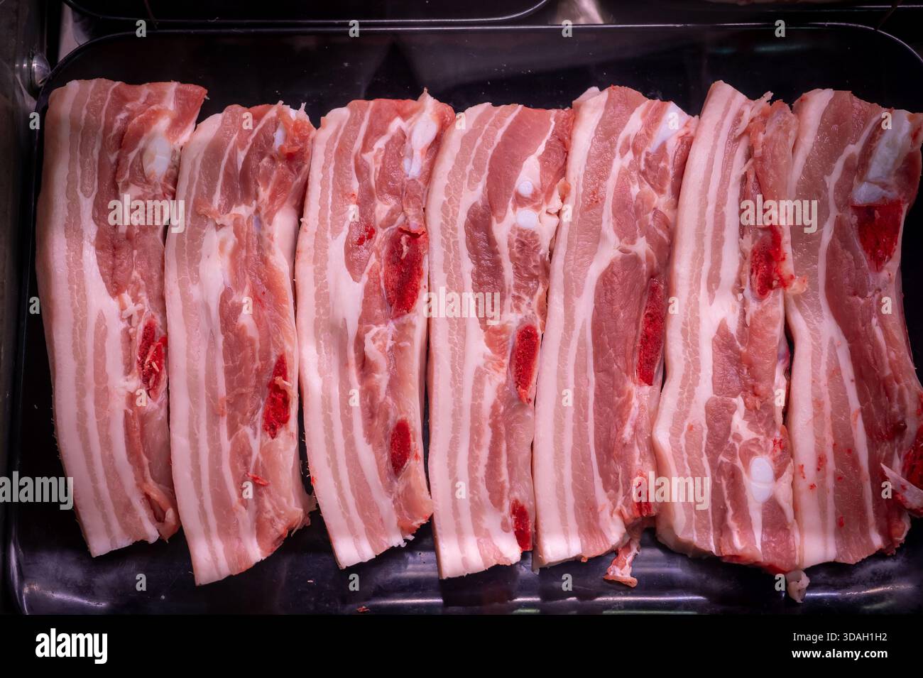 Uno scatto ravvicinato mostra le fette di bacon crude disposte ordinatamente su un vassoio di plastica nero Foto Stock