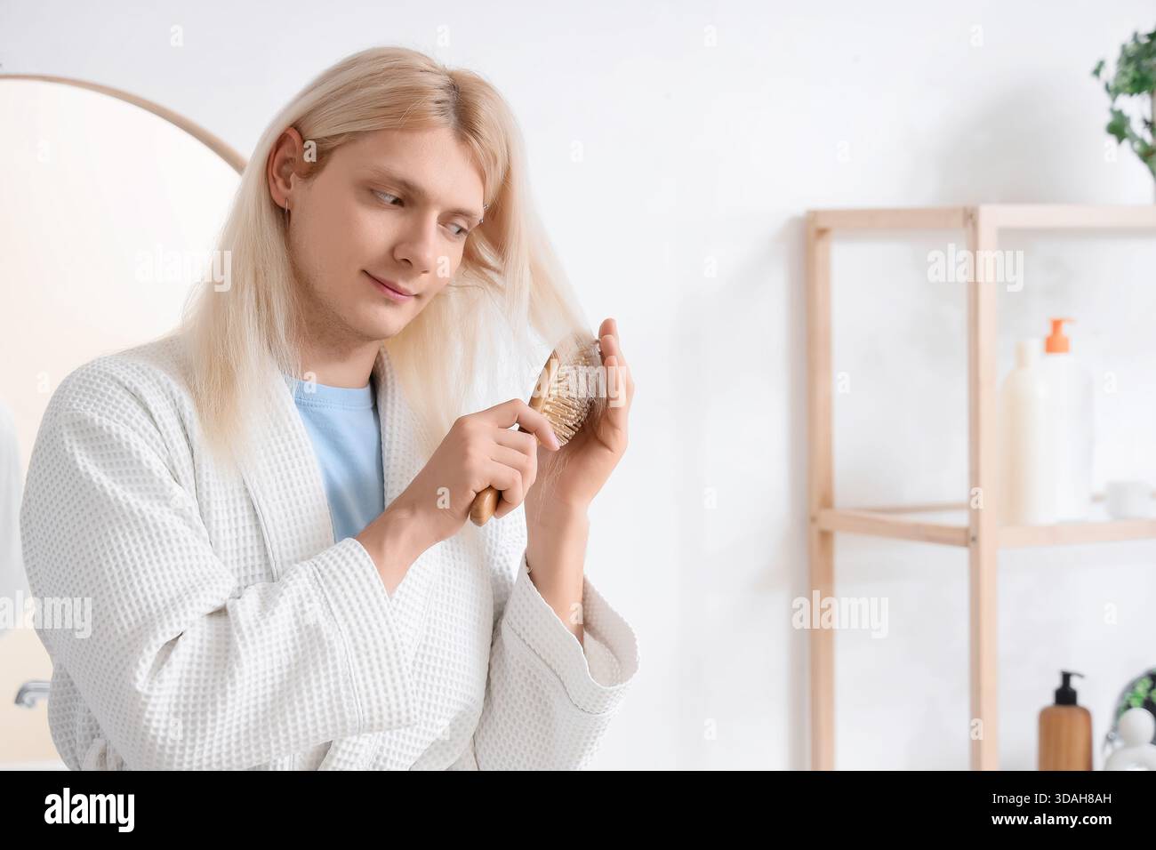 Giovane uomo biondo che pulisce i capelli in bagno Foto Stock