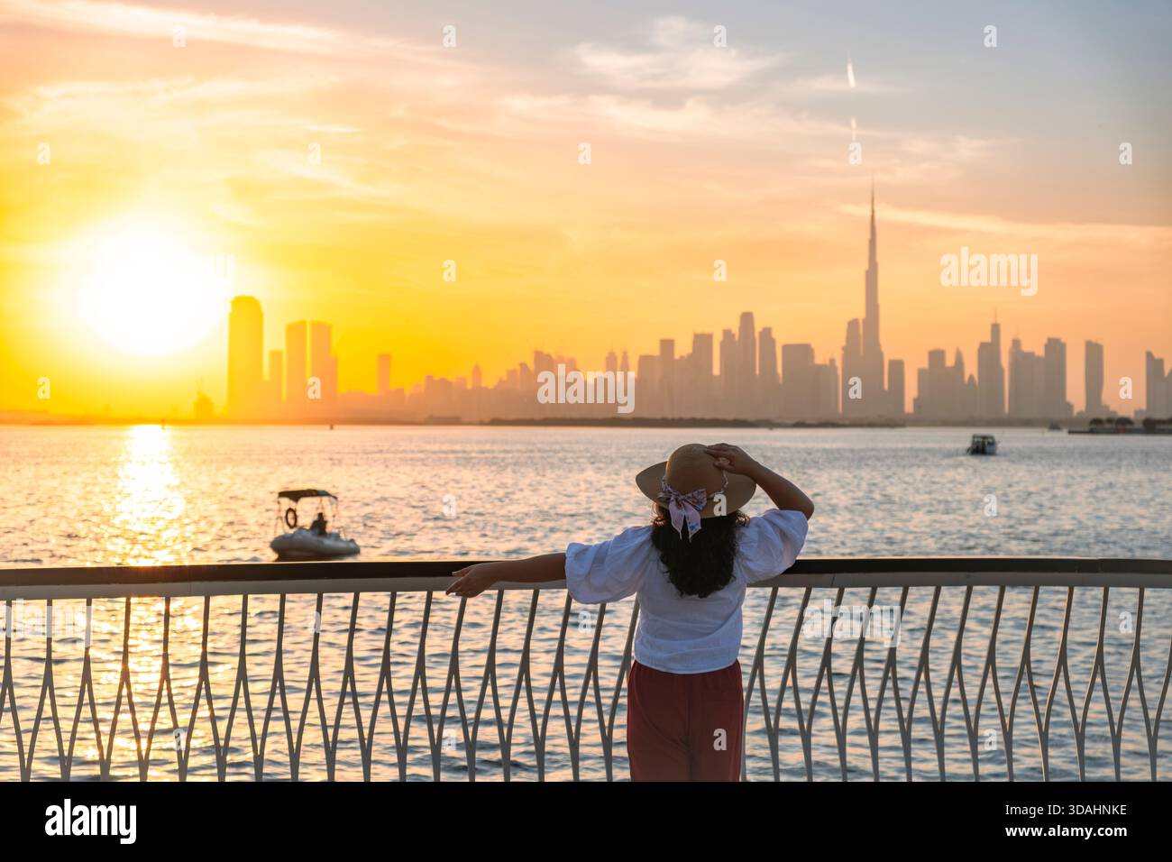 Giovane donna turistica che guarda lo skyline di Dubai al tramonto con le barche nel porto di Dubai creek, viaggi da solo e immagine turistica Foto Stock