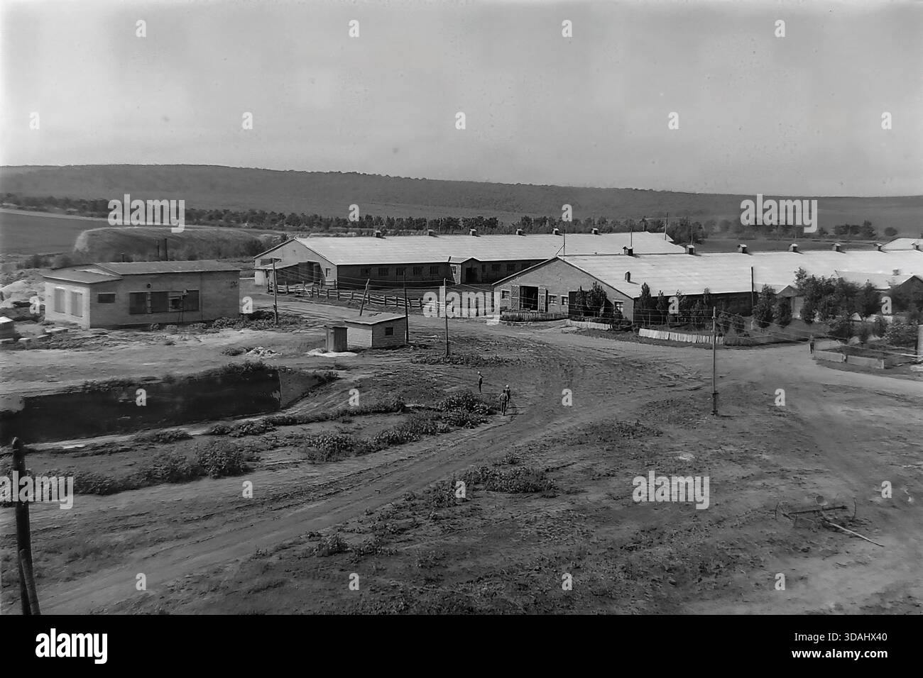 Bohorodychne, regione di Donetsk, RSS Ucraina, anni 1970 Una vista panoramica archivistica di un grande complesso agrituristico situato in una valle vicino alle colline. Lunghe stalle in mattoni e stalle con tetti in ardesia sono disposte intorno a cortili di sterrato. In primo piano, i cavalli sono visti in coralli di legno, mentre i materiali da costruzione suggeriscono lo sviluppo continuo delle infrastrutture rurali. Questo paesaggio cattura le dimensioni dell'allevamento e l'atmosfera tranquilla della campagna sovietica nel Donbas. Foto Stock