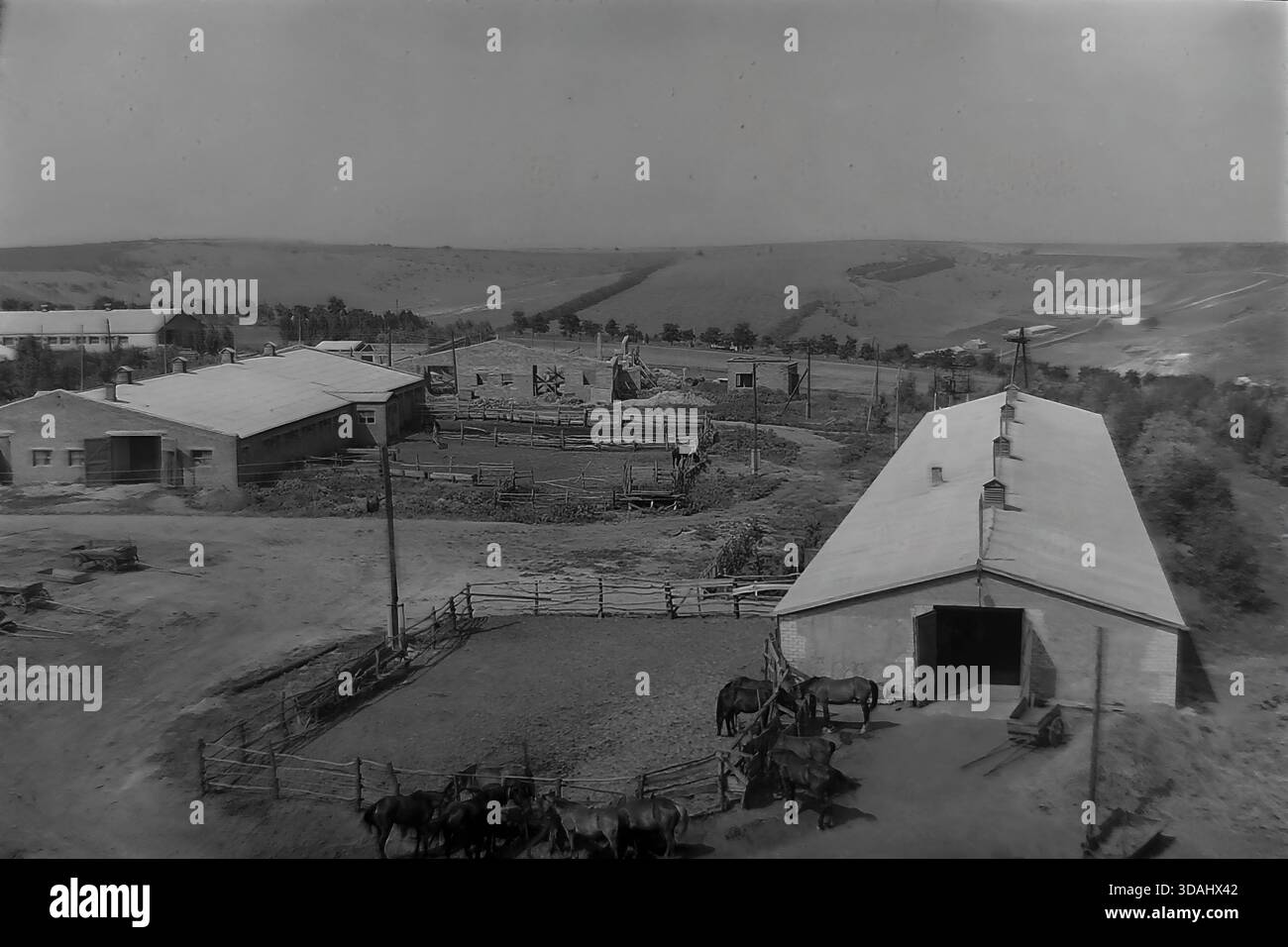 Bohorodychne, regione di Donetsk, RSS Ucraina, anni 1970 Una vista panoramica archivistica di un grande complesso agrituristico situato in una valle vicino alle colline. Lunghe stalle in mattoni e stalle con tetti in ardesia sono disposte intorno a cortili di sterrato. In primo piano, i cavalli sono visti in coralli di legno, mentre i materiali da costruzione suggeriscono lo sviluppo continuo delle infrastrutture rurali. Questo paesaggio cattura le dimensioni dell'allevamento e l'atmosfera tranquilla della campagna sovietica nel Donbas. Foto Stock