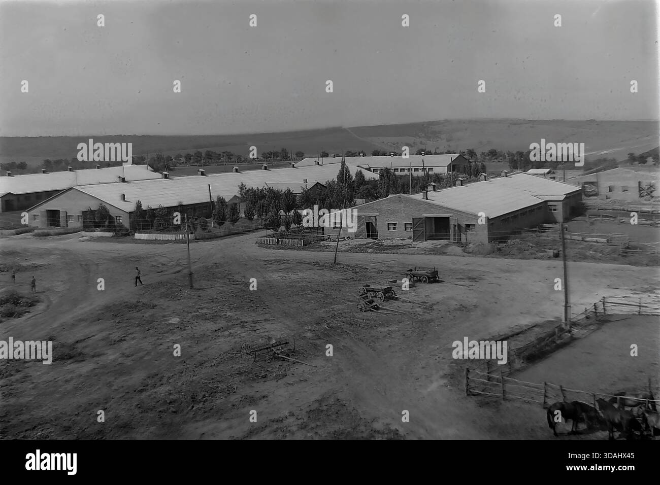 Bohorodychne, regione di Donetsk, RSS Ucraina, anni 1970 Una vista panoramica archivistica di un grande complesso agrituristico situato in una valle vicino alle colline. Lunghe stalle in mattoni e stalle con tetti in ardesia sono disposte intorno a cortili di sterrato. In primo piano, i cavalli sono visti in coralli di legno, mentre i materiali da costruzione suggeriscono lo sviluppo continuo delle infrastrutture rurali. Questo paesaggio cattura le dimensioni dell'allevamento e l'atmosfera tranquilla della campagna sovietica nel Donbas. Foto Stock