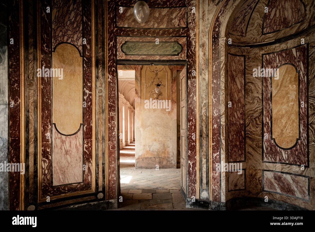 AGLIÈ, ITALIA – OTTOBRE 2025: Vista interna del castello di Agliè con pareti dipinte ornate, marmi invecchiati e porte che conducono a un corrido illuminato dal sole Foto Stock