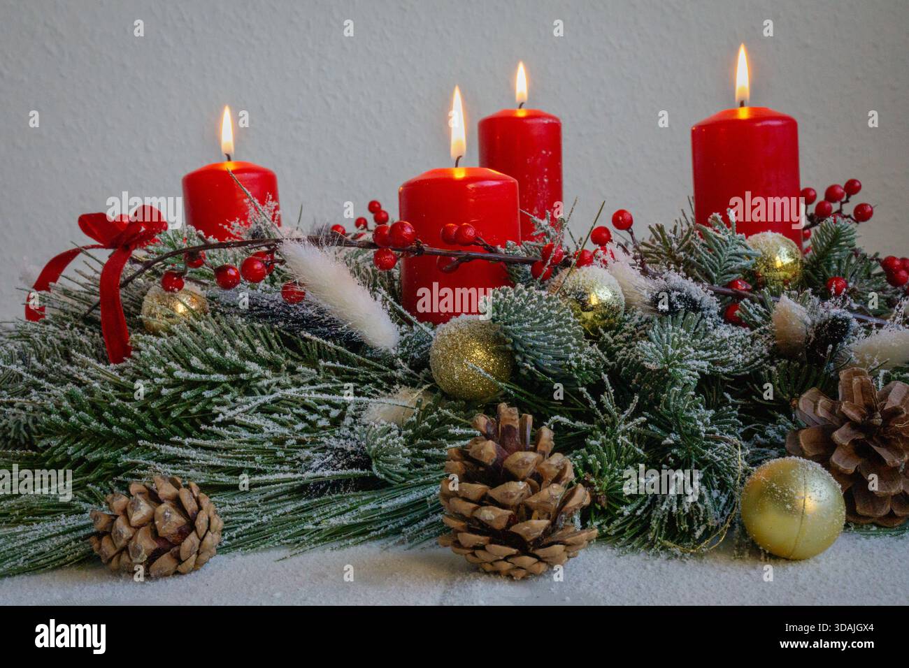 Una candela rossa scintillante si erge tra rami sempreverdi smerigliati, agrifoglio e frutti di bosco luminosi su una superficie rustica in legno. Foto Stock