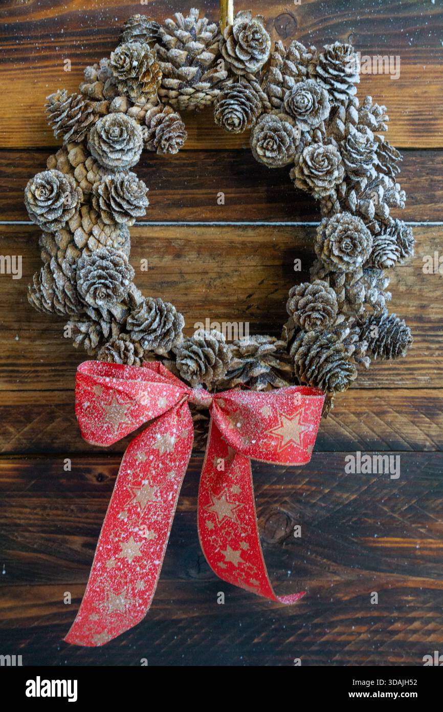 Una corona di pinecone fatta a mano è appesa su uno sfondo rustico in legno, leggermente smerigliato per un look invernale. Foto Stock