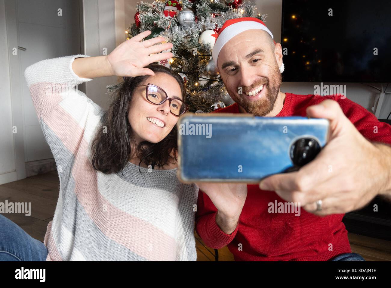 Coppia che effettua una videochiamata con l'albero di Natale nel salotto Foto Stock