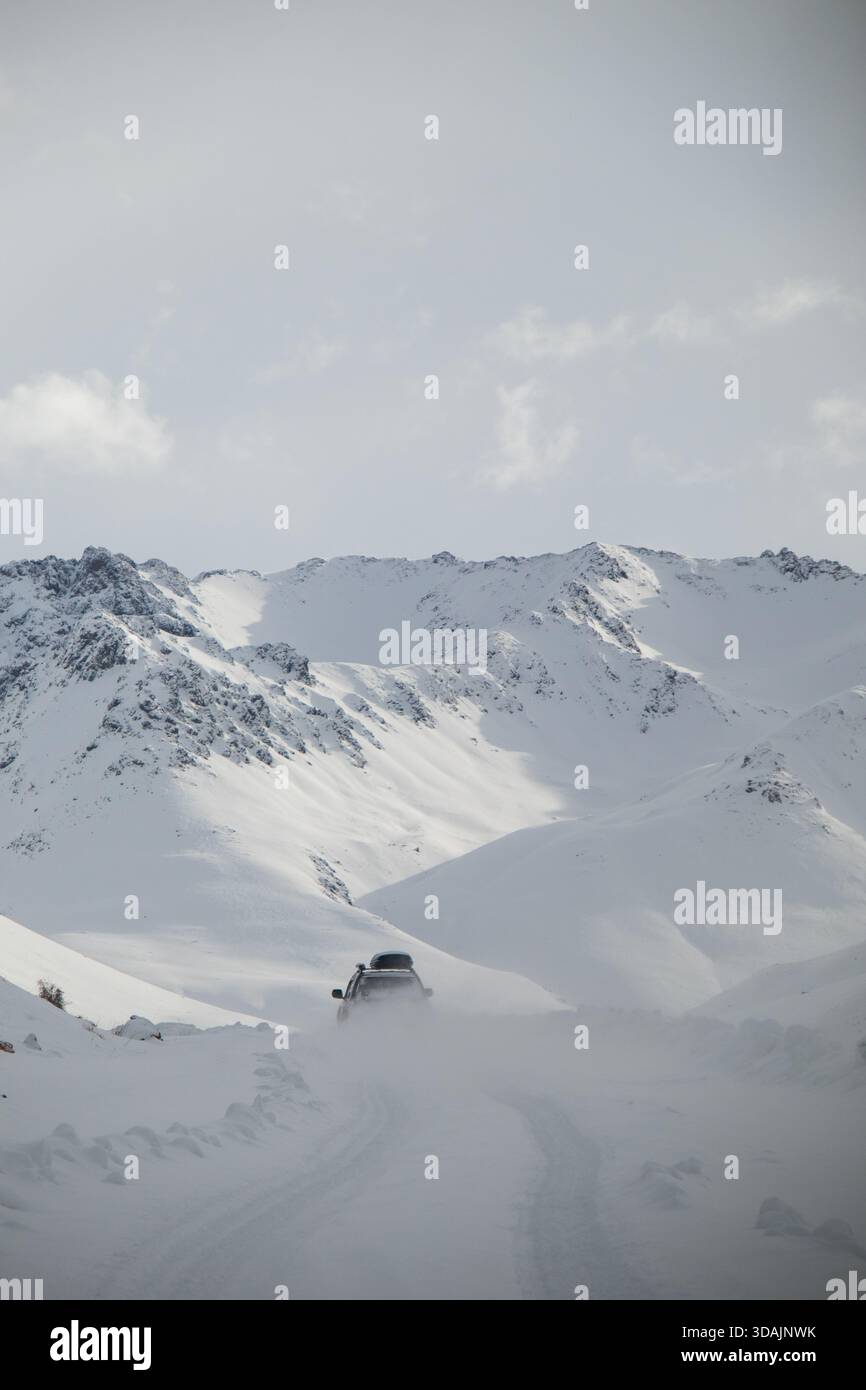 Vista posteriore di un veicolo fuoristrada che guida su una pista innevata lasciando una scia di polvere di neve sulle montagne Foto Stock