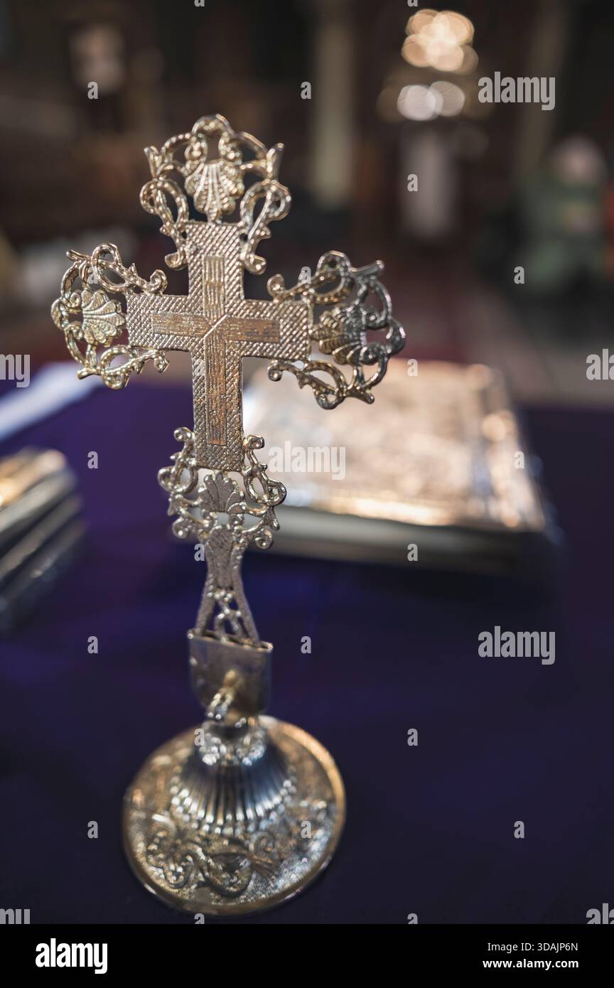 Petrosani, Romania, 22 novembre 2025: Croce d'argento ornata su un telo liturgico viola profondo libro religioso rilegato in argento sfondo sfocato Foto Stock