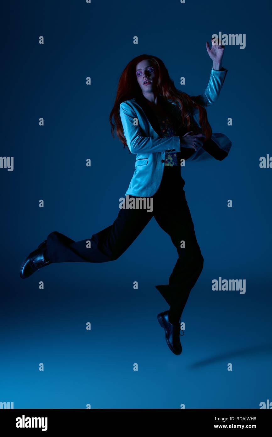 Una persona vestita con stile salta con gioia, celebrando orgoglio e identità in una scena artistica. Foto Stock