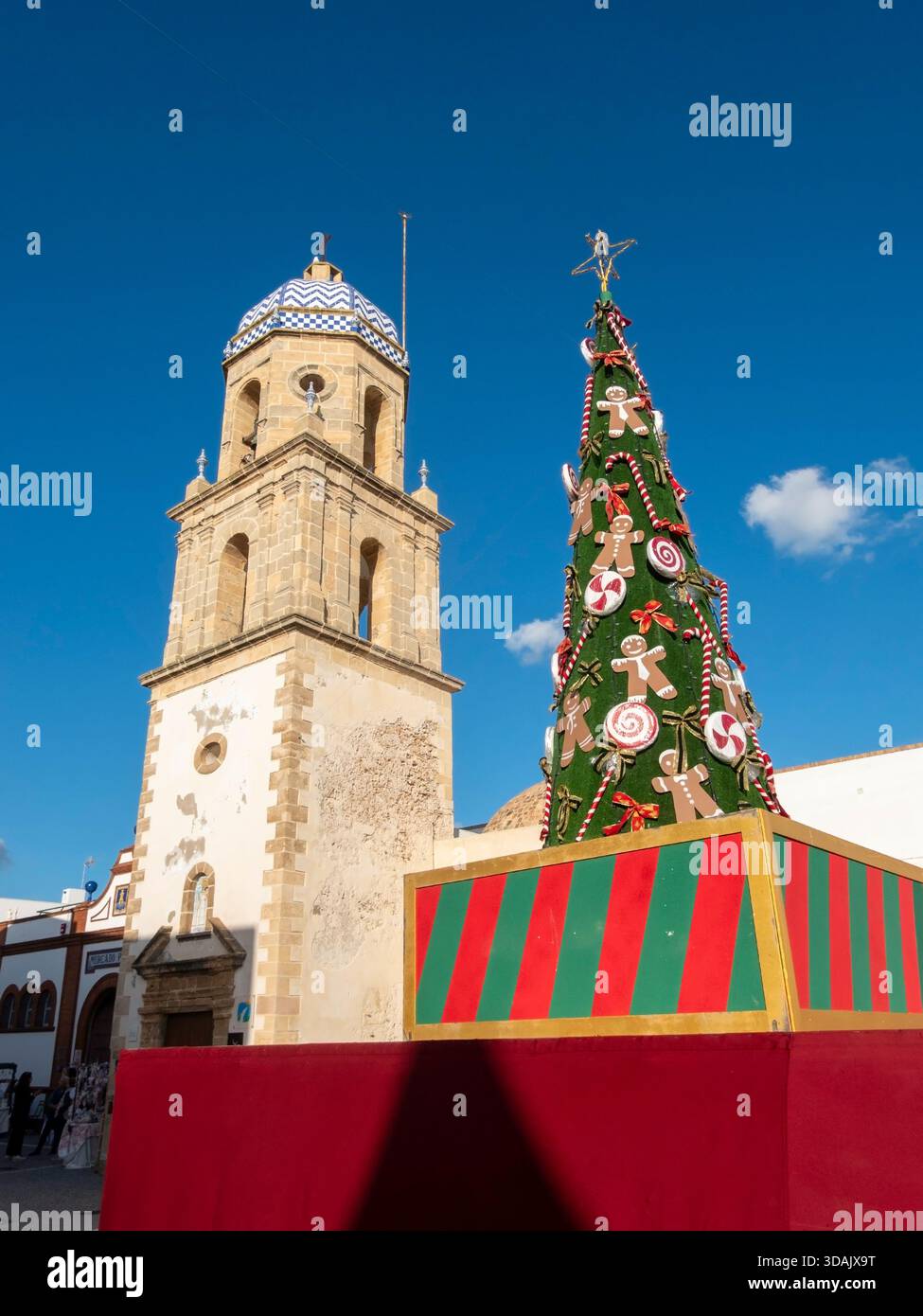 Rota, Cadice, Spagna - 7 dicembre 2025: Festoso albero di Natale all'aperto decorato con grandi ornamenti di caramelle, figure di pan di zenzero e una stella dorata Foto Stock