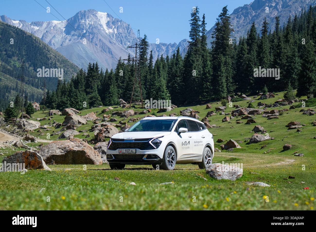 Regione di Naryn, Kirghizistan - 13 maggio 2024: Vista frontale del suv bianco Kia Sportage parcheggiato su un prato verde con rocce sparse e montagne innevate Foto Stock