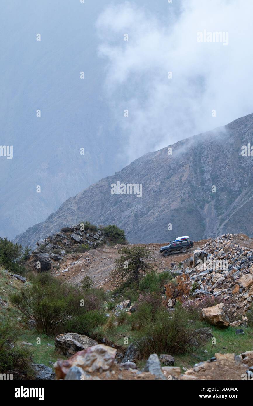 Regione di Naryn, Kirghizistan - 13 maggio 2024: Un'auto da spedizione si erge su un passo roccioso di montagna con spettacolari nuvole e nebbia sullo sfondo Foto Stock