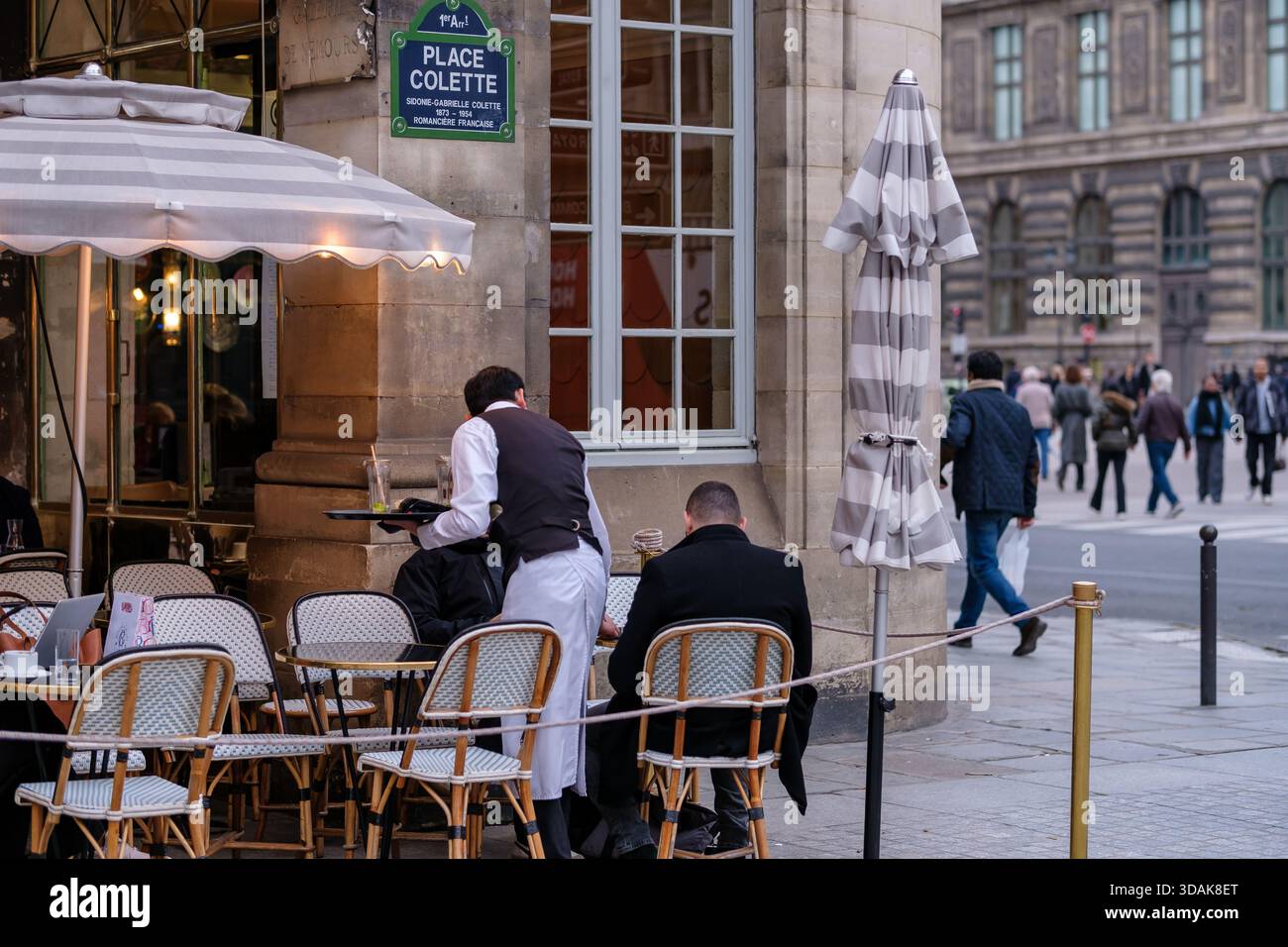 Parigi, Francia - 10 dicembre 2025: Veduta di un caffè tipico e di un cameriere che serve un tavolo con i clienti in Place Colette a Parigi Francia Foto Stock