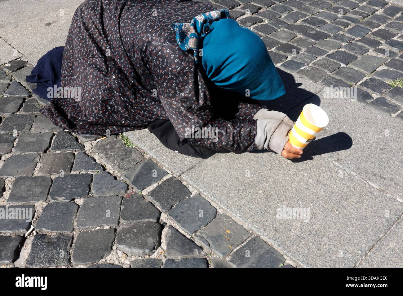 Donna prostrata su ciottoli vicino alla zona turistica, in cerca di elemosine con tazza di carta. Foto Stock