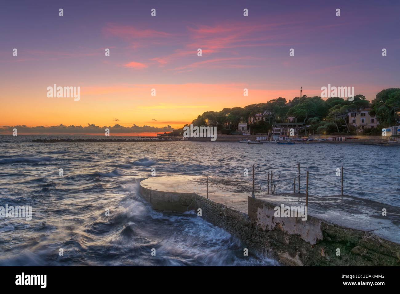 Splendida vista al tramonto sul lungomare di Castiglioncello, Toscana, Italia, con un molo o una piattaforma in cemento che si estende fino all'acqua. Le onde si infrangono intorno a t Foto Stock