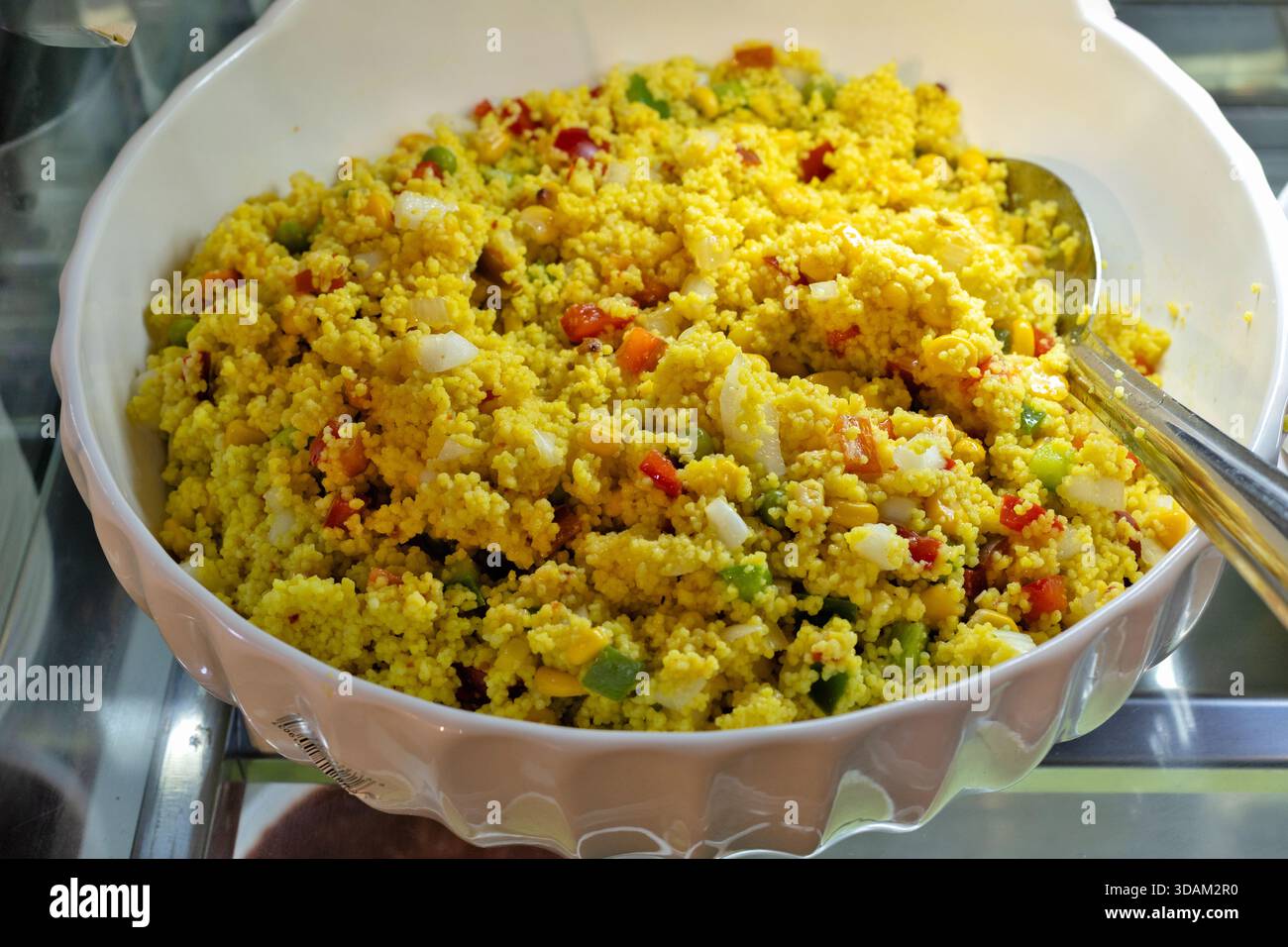 Un'insalata di couscous vibrante e nutriente è presentata in un grande recipiente bianco da portata, con peperoni, cipolle e chicchi di mais tritati finemente. Foto Stock