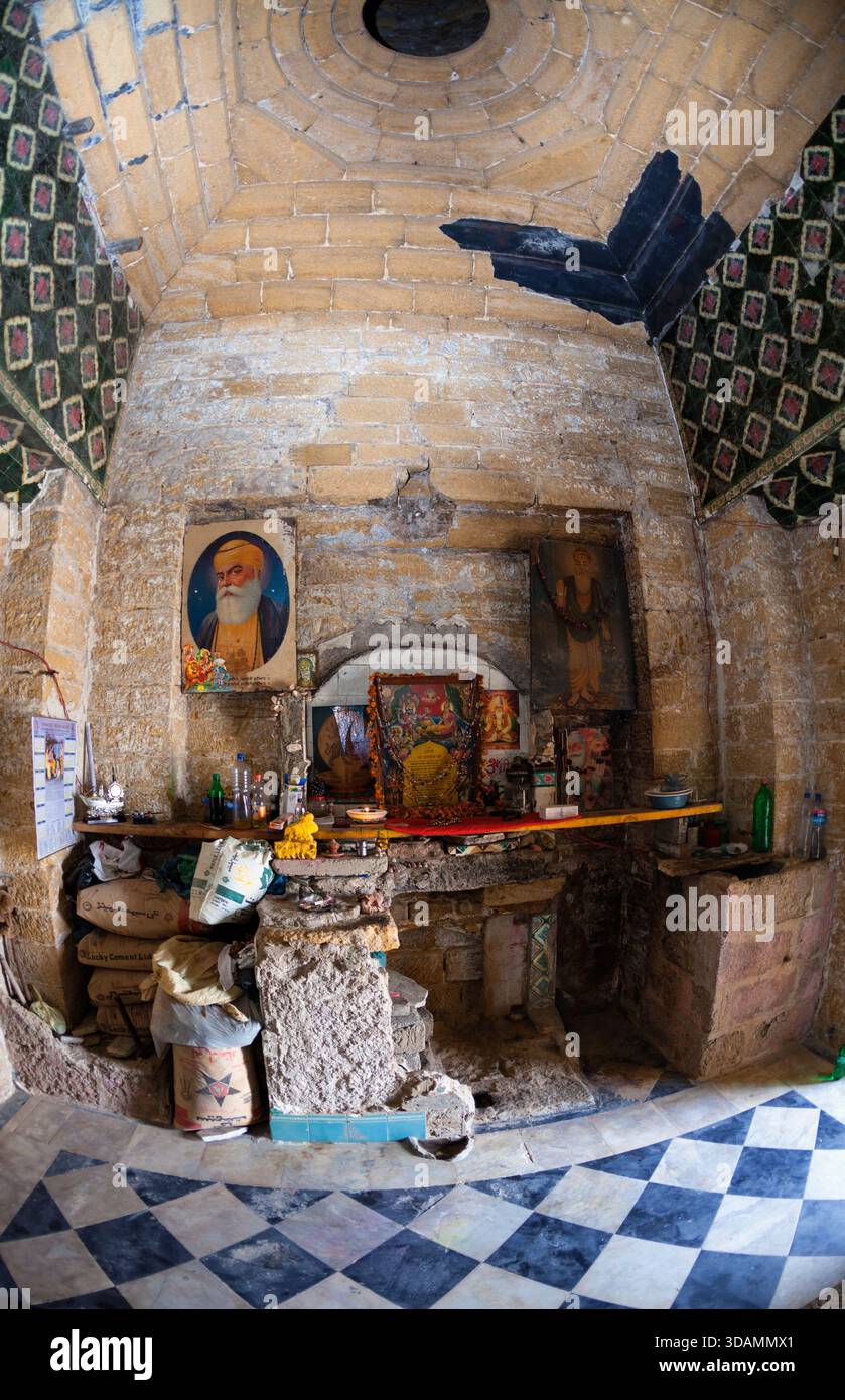 La vista di uno spazio interno con pavimenti a scacchi, iconografia religiosa e pareti sbriciolate evoca un senso di storia e degrado, Karachi, Sindh, Pakis Foto Stock