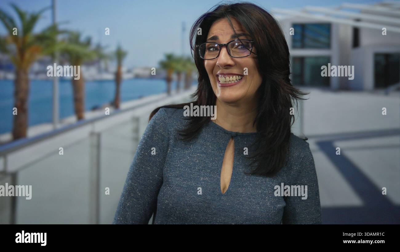 Una donna che indossa gli occhiali sgombra e abbassa lo sguardo sul passaggio pedonale del porto sul mare da un edificio bianco; tranquilla e malinconica solitudine. Foto Stock