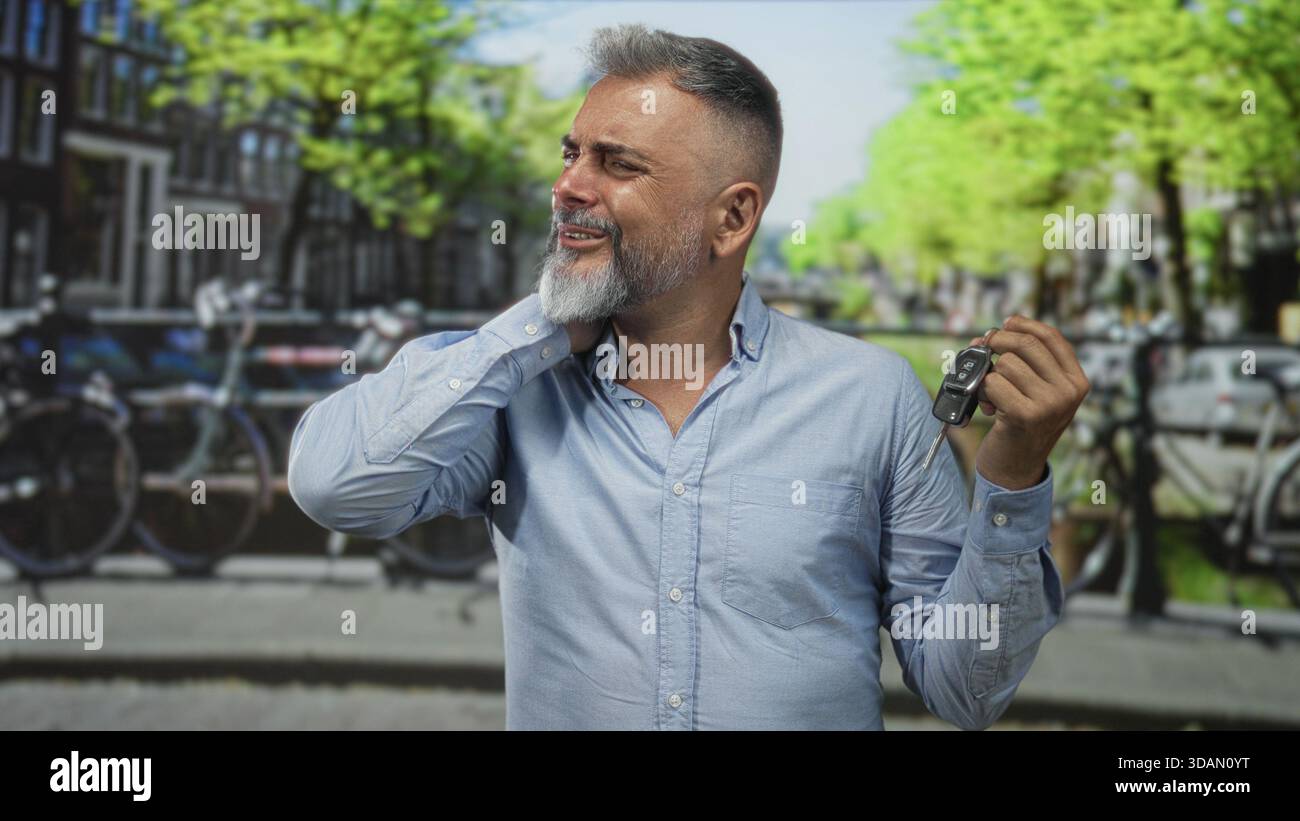 Uomo che tiene in mano la chiave della macchina con la mano sul collo per dolore al collo per strada ad amsterdam, accanto al canale; disagio per gli effetti personali persi. Foto Stock