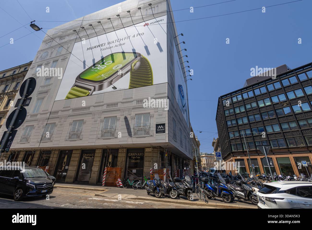MILANO, ITALIA, 06.19.2025: Un imponente cartellone Huawei Watch Fit 4 Pro domina un edificio in pietra bianca mentre una vivace scena stradale della città si svolge in auto Foto Stock