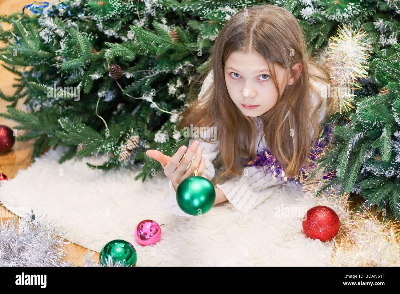 Preadolescenti sdraiati in mezzo a biglie e tinsel, che si estendono dalla mano alla palla verde lucente vicino agli alberi di Natale. Foto Stock