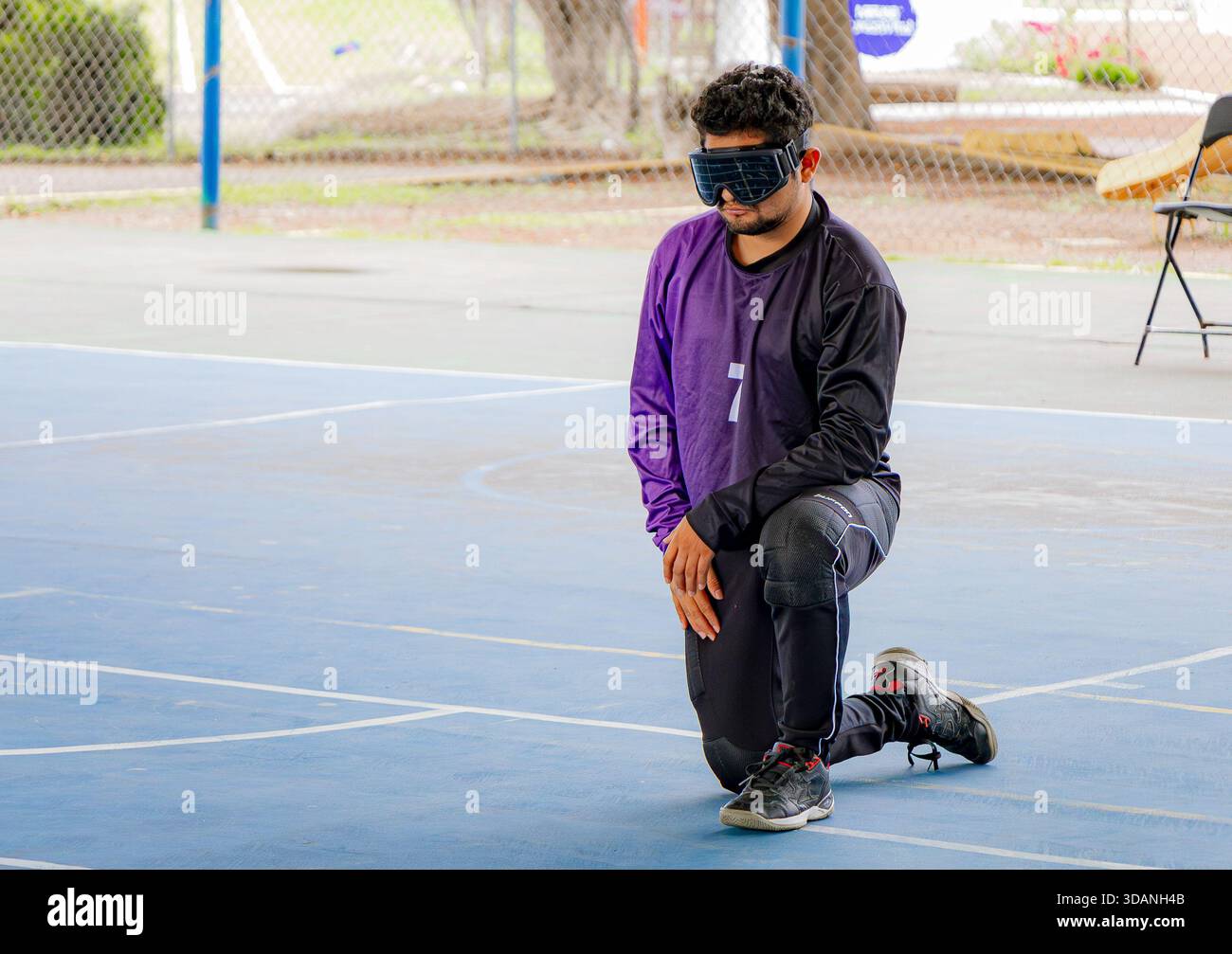 Giocatore di pallacanestro cieco inginocchiato in una posizione di attesa o difensiva su un campo sportivo blu. Rappresenta la concentrazione e la calma. Foto Stock