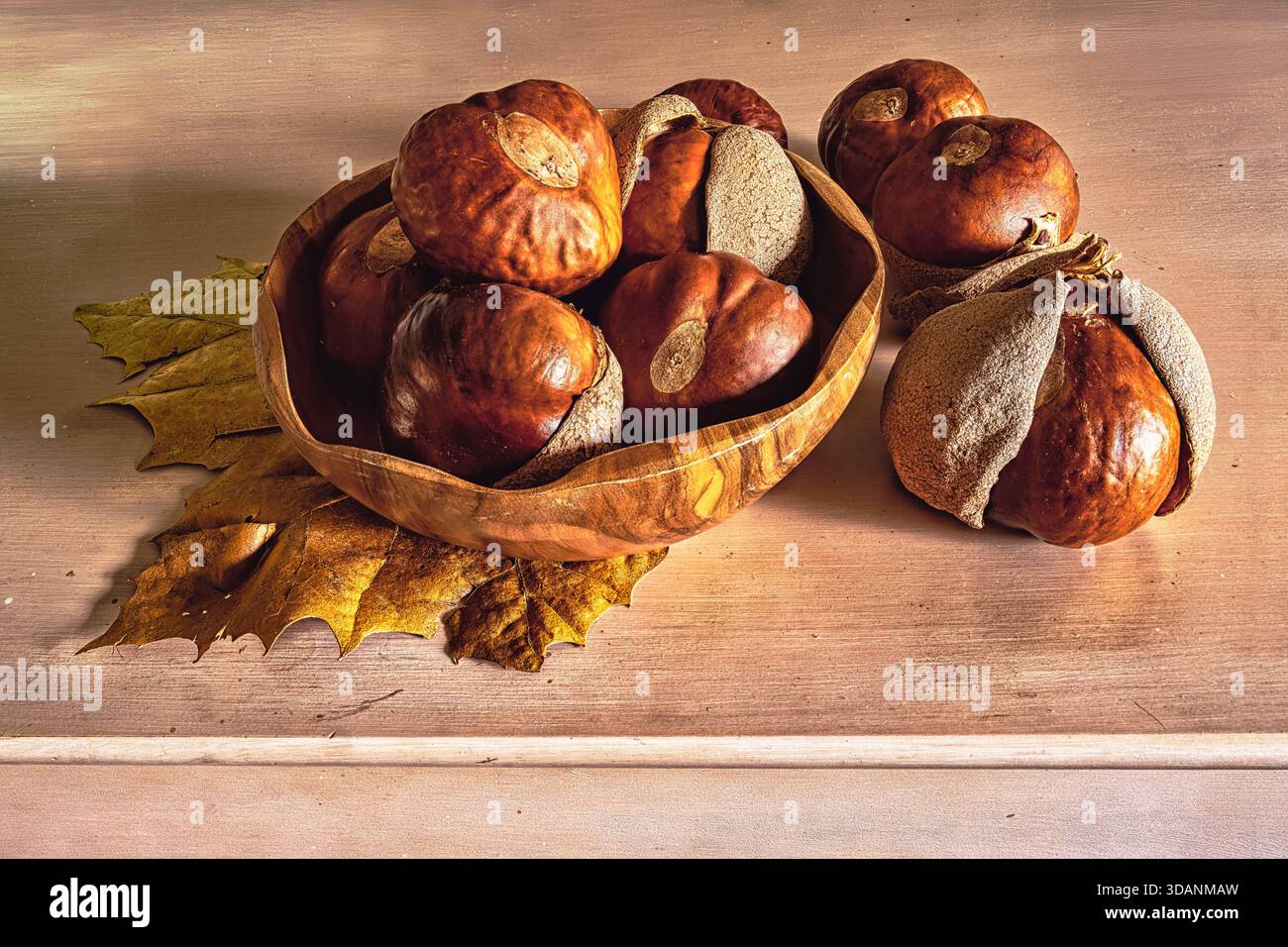 Castagne in una ciotola di legno su un tavolo con foglie autunnali. Concetto di cucina tradizionale. Foto Stock