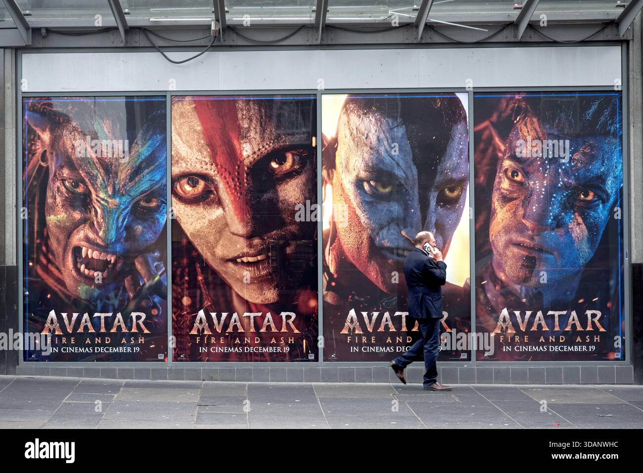 Uomo al telefono che cammina accanto a un cinema che pubblicizza il film Avatar - fuoco e cenere. Foto Stock