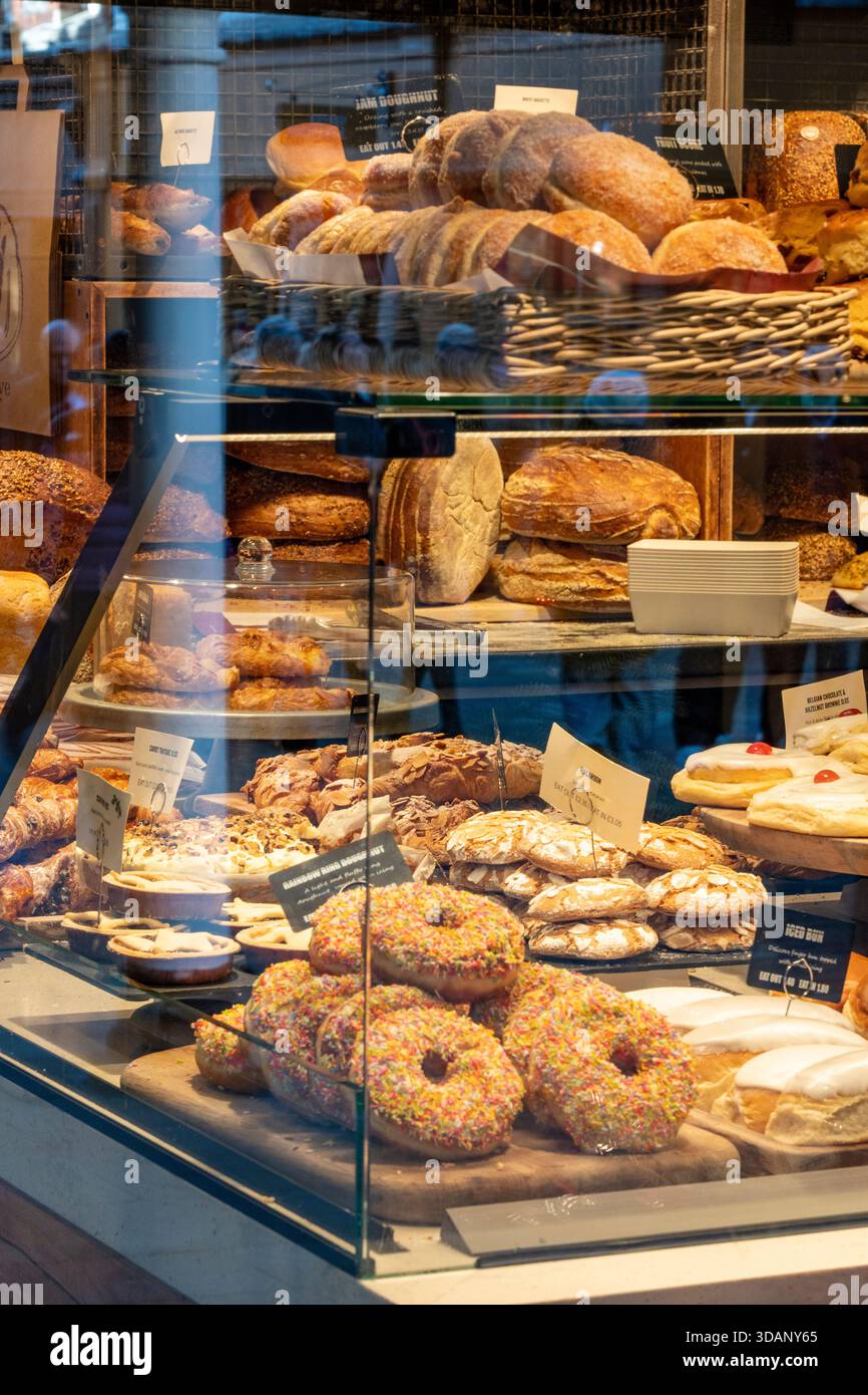 Torte, ciambelle e pane appena sfornati nella finestra di una panetteria artigianale nel centro di Winchester. Foto Stock