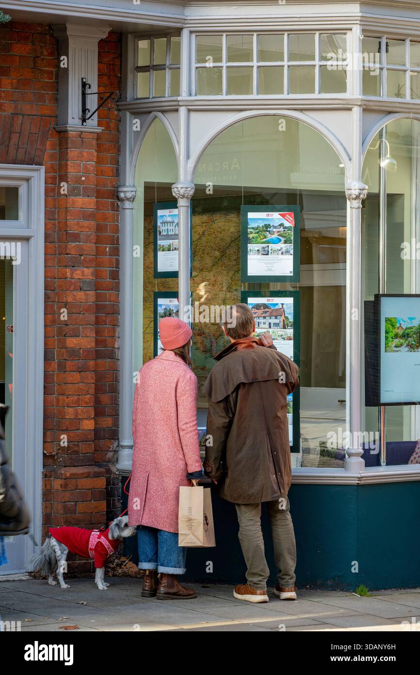 Coppia di mezza età con cane da compagnia che guarda alla finestra di un agente immobiliare nella città di Winchester, Hampshire, Regno Unito Foto Stock