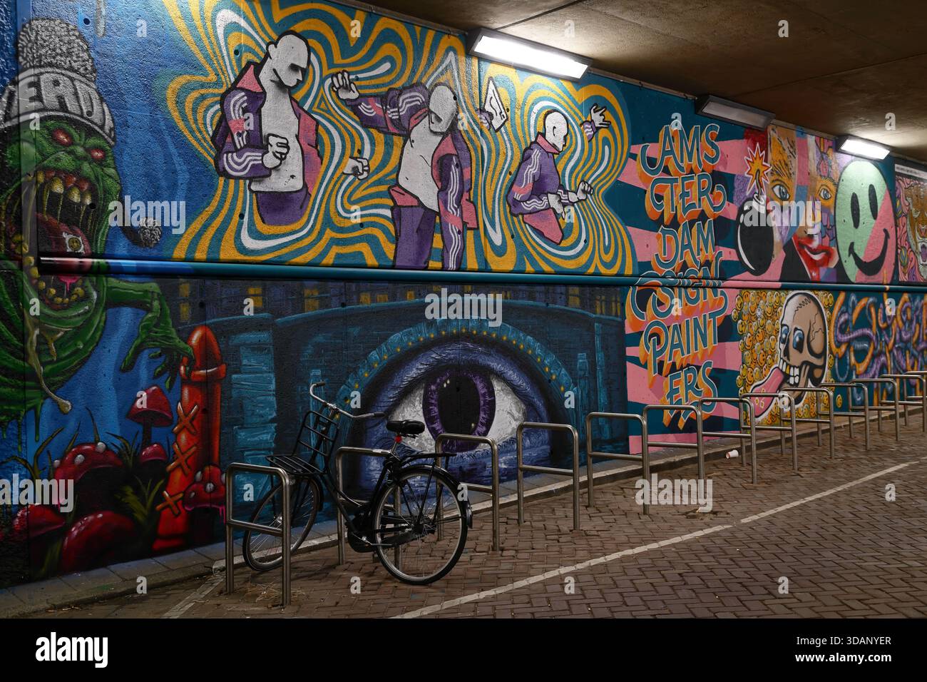 Muro murale con figure, grande occhio e Amsterdam Street Painters testo in portabiciclette nel tunnel di Dijksgracht, Amsterdam, Paesi Bassi, di notte. Foto Stock