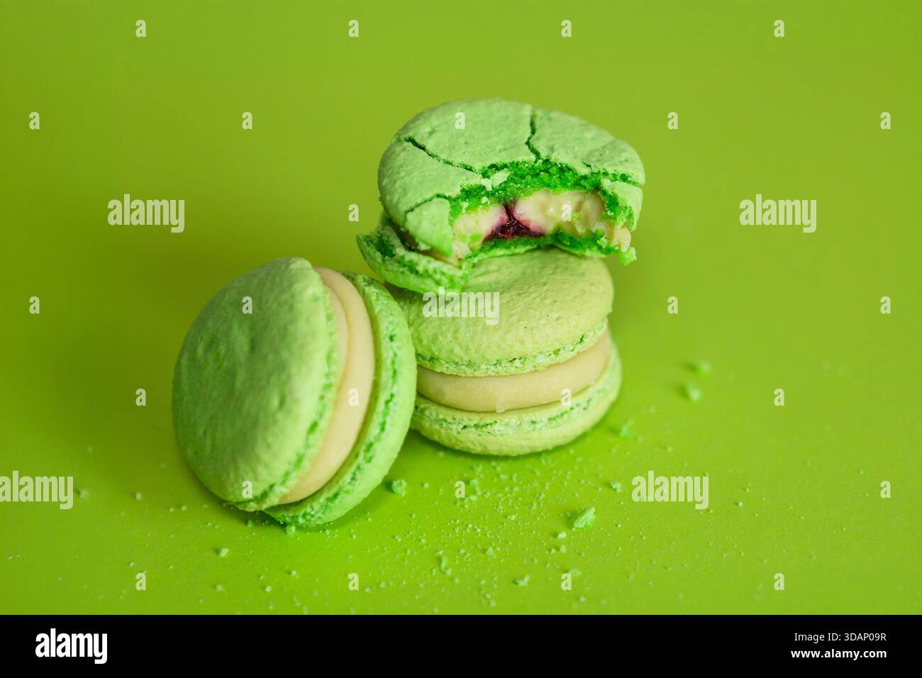 diversi macaron verdi su sfondo verde, uno dei quali è morso e le briciole sono sparse intorno Foto Stock