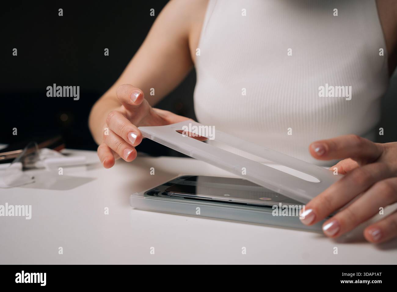 Tecnico qualificato donna che utilizza una macchina specializzata per applicare con precisione la pellicola protettiva in vetro sullo schermo dello smartphone, garantendo la massima copertura e. Foto Stock