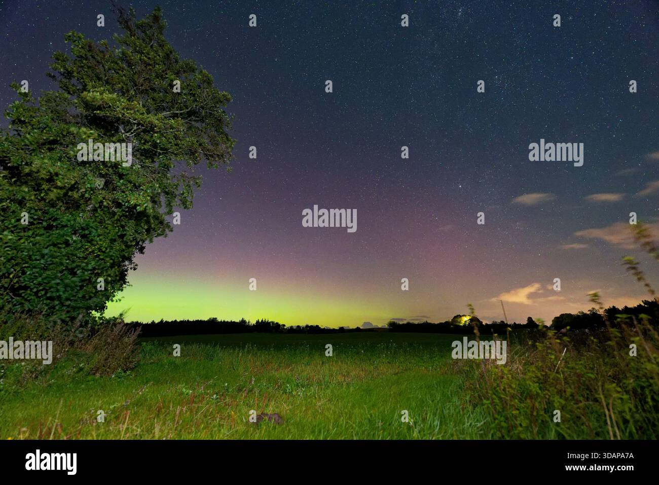 Veli di colore oscillano sopra i campi scuri e il cielo diventa spazioso e gentile, la luce delicata si deposita sull'erba e sul terreno mentre l'orizzonte lontano tiene il suo basso Foto Stock