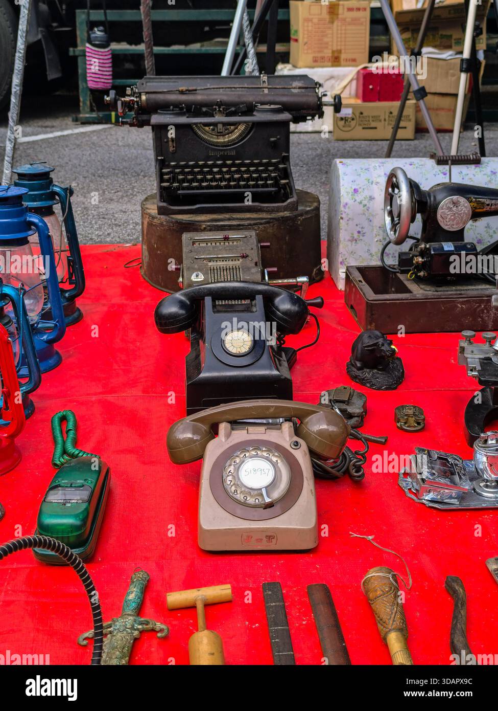 IPOH, MALESIA - 9 NOVEMBRE 2025: Telefoni vintage, lanterne e una macchina da scrivere antica sono esposti su un panno rosso in una bancarella del mercato. Foto Stock