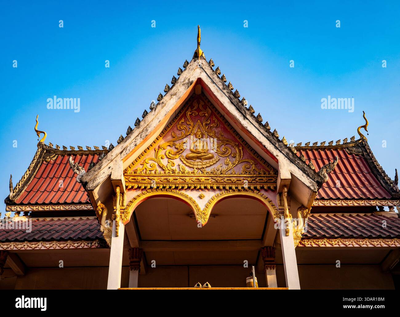 Tradizionale tetto thailandese con decorazioni dorate ornamentali su un cielo blu chiaro. Foto Stock