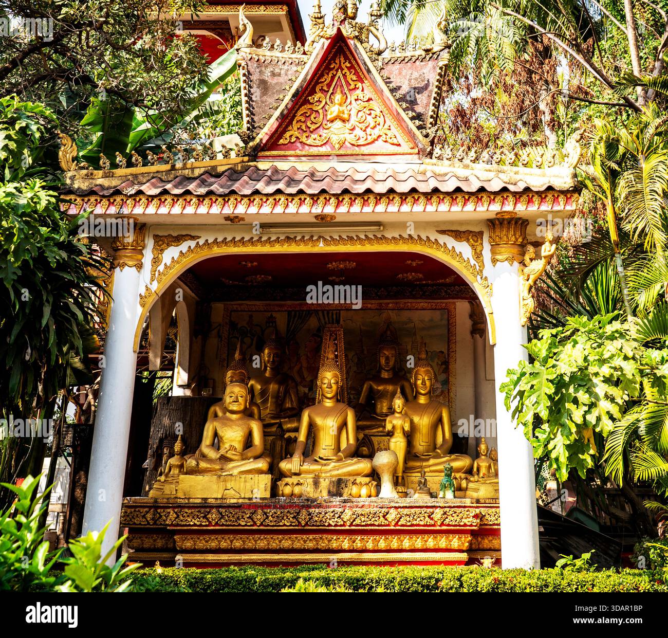 Un gruppo di statue dorate di Buddha in un santuario esterno ornato circondato da lussureggiante vegetazione. Foto Stock