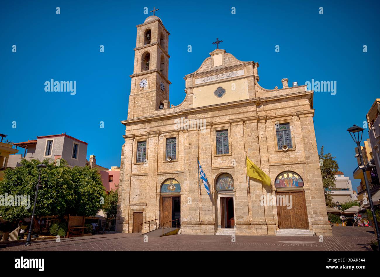 Chiesa di San Nicola nel centro storico di Chania, Creta, Grecia, con facciata in pietra, campanile, e bandiere greche sotto il cielo blu. Foto Stock