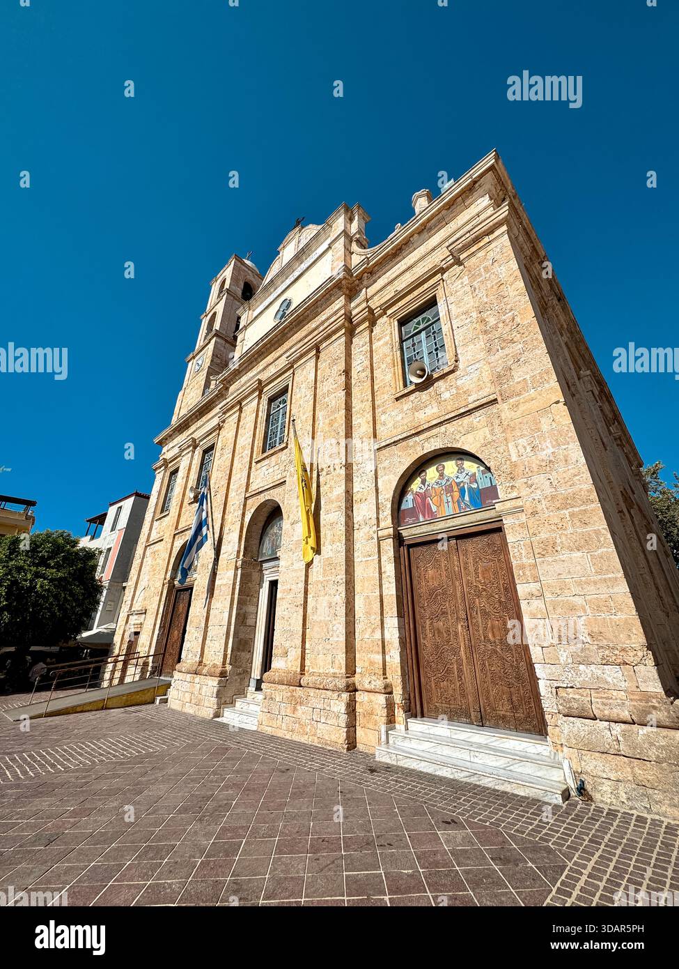 Chiesa di San Nicola nel centro storico di Chania, Creta, Grecia, con facciata in pietra, campanile, e bandiere greche sotto il cielo blu. Foto Stock