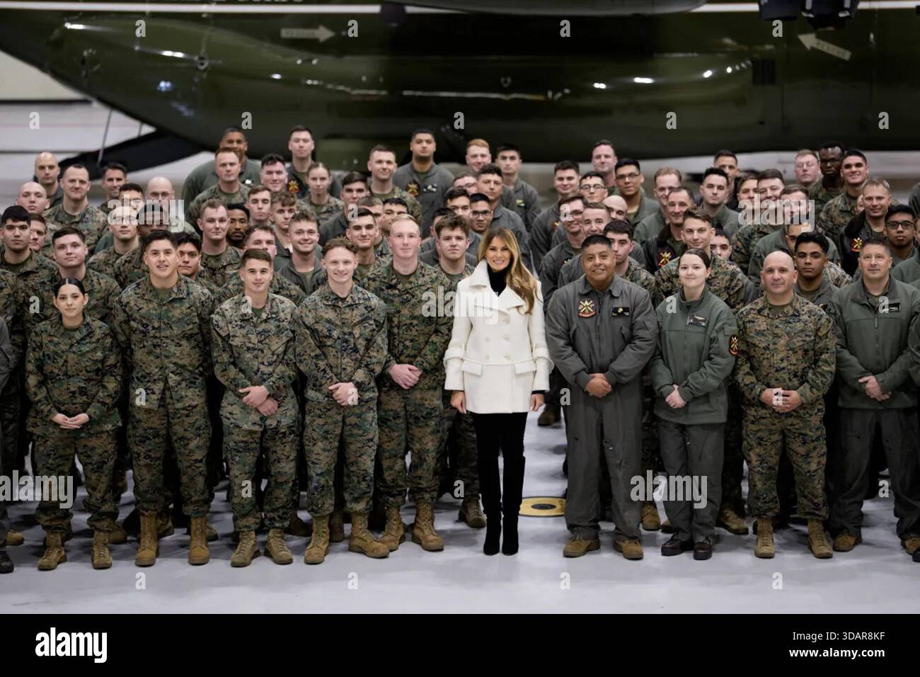 La First Lady Melania Trump posa per una foto di gruppo con i Marines e il personale degli Stati Uniti durante un evento natalizio Toys for Tots alla base dei Marines di Quantico, con un elicottero del corpo dei Marines nell'hangar dietro di loro. Marine Corps base Quantico, Quantico, Virginia, USA. 8 dicembre 2025. Per gentile concessione della Casa Bianca. Foto Stock