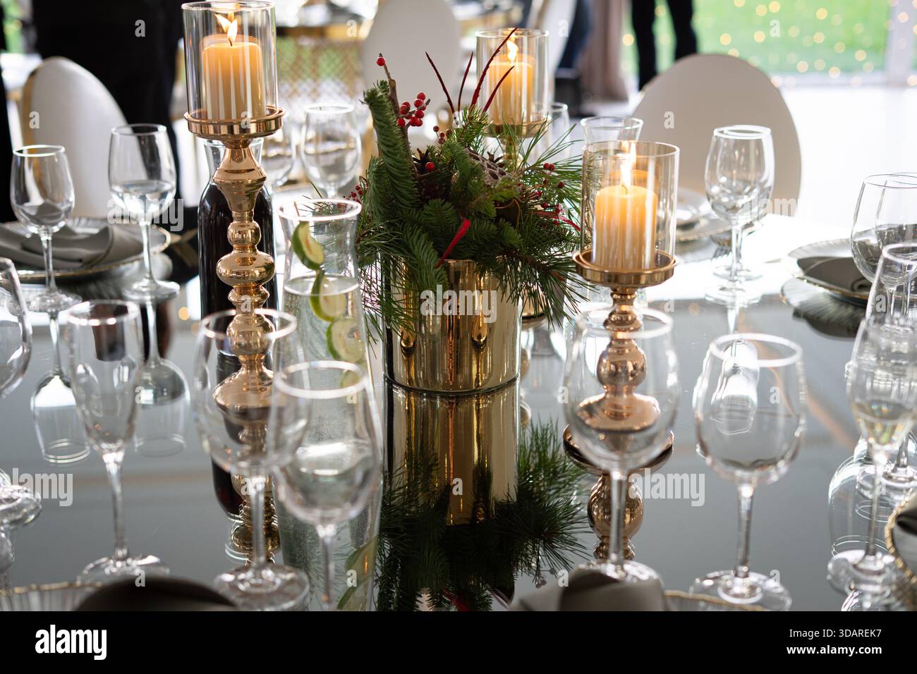 Un tavolo da pranzo festoso decorato con candele, bicchieri e un pezzo centrale di verde e frutti di bosco in un ambiente riflettente. Foto Stock