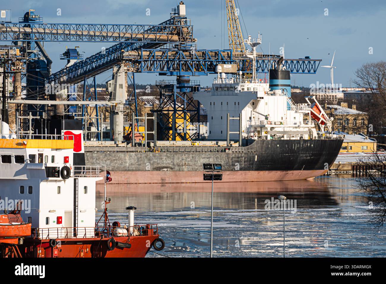 Ventspils, Lettonia, 6 febbraio 2021: Grande nave da carico a fianco di un'altra nave in un porto industriale affollato in condizioni climatiche fredde e chiare Foto Stock